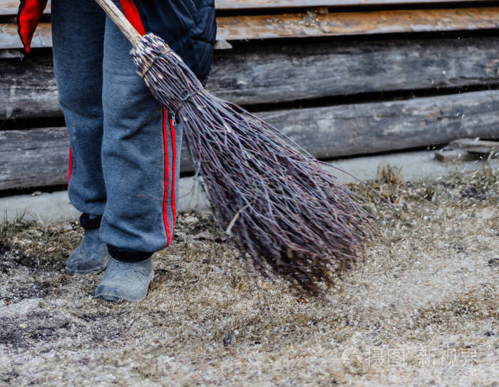 一个村子里的女人用桦树扫帚打扫她家附近的院子