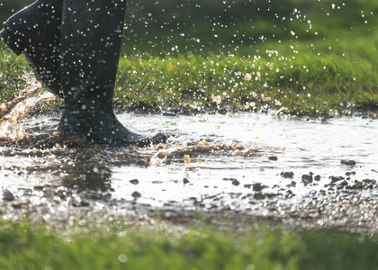 person walking in a large muddy puddle with boots 