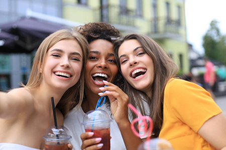 三个时髦的时髦女孩，朋友们在都市背景下喝鸡尾酒。