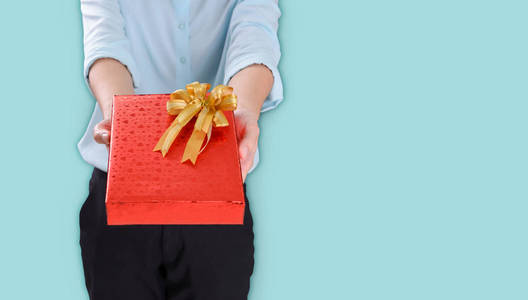女性手拿礼物，红色包装礼盒装饰有金色丝带，用于节日圣诞节感谢日生日，蓝色背景，带复印空间