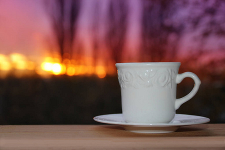 客厅鞋柜茶水间白色的咖啡杯里,茶水的背景是傍晚紫色的夕阳映在树枝