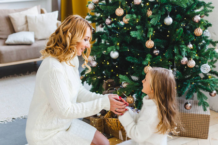 一个女孩和妈妈在圣诞树旁，室内装饰着新年和圣诞节，家人和欢乐，传统