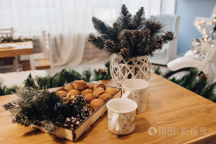 餐桌上的开胃纸杯蛋糕和马克杯，在舒适室内提供圣诞装饰