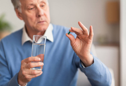 老人拿着药丸和一杯水在室内