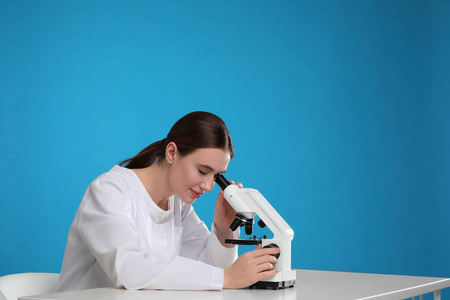 科学家在餐桌上用现代显微镜对着蓝色背景