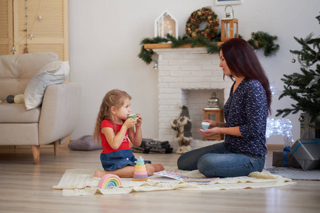 母亲和女儿的画像，妈妈和女儿正在家里的地板上玩耍。内部圣诞节或新年