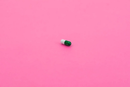 上瘾的粉红色一个粉红色背景的白色绿色小胶囊.医疗照片