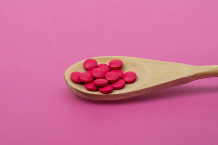 粉红色背景的木制勺子里的粉红色药丸。特写
