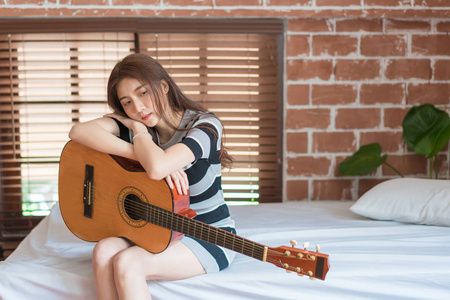 Portrait of Asian young woman sitting on bed and playing guitar 