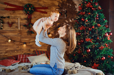 年轻的母亲在圣诞树旁和婴儿玩耍照片