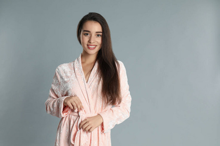 Beautiful young woman in bathrobe on grey background. Space for 
