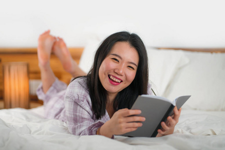 年轻美丽甜美的亚洲华裔女性，在床上看书看小说开心好玩，或在家里学习，穿着可爱的睡衣，显得温馨而亲切