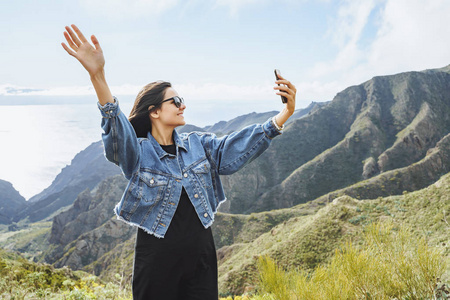 一个年轻的女人在用智能手机自拍群山和一个年轻的旅行者。