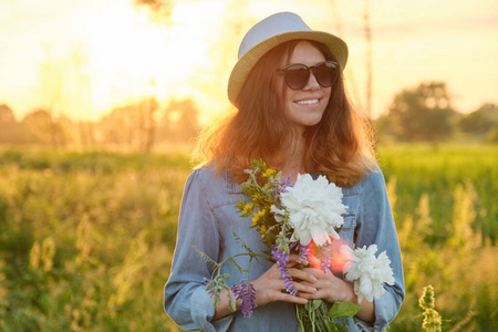 草地上快乐的少女戴着眼镜，戴着帽子，带着一束鲜花