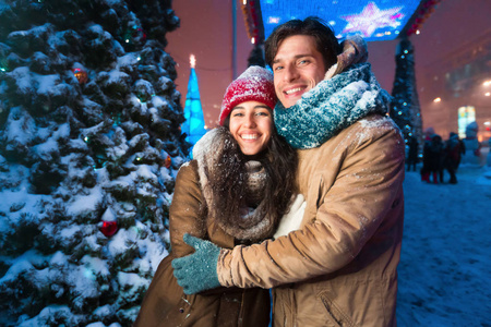 一对快乐的情侣微笑着站在城市的圣诞树旁