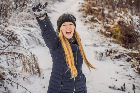 冬天的女孩向镜头扔雪球微笑着快乐地在下雪的冬日户外玩耍。可爱俏皮的年轻女子在户外享受初雪