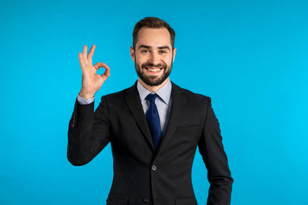 Positive young businessman smiles to camera. Man showing OK sign