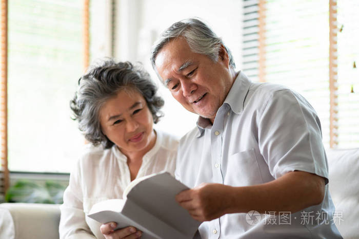 一对亚洲老年夫妇坐在沙发上看书。