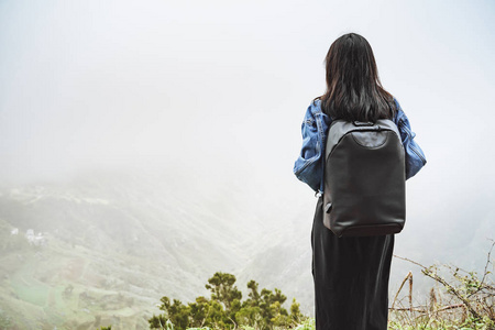 背着背包的年轻女游客在山顶上放松，欣赏雾谷的景色