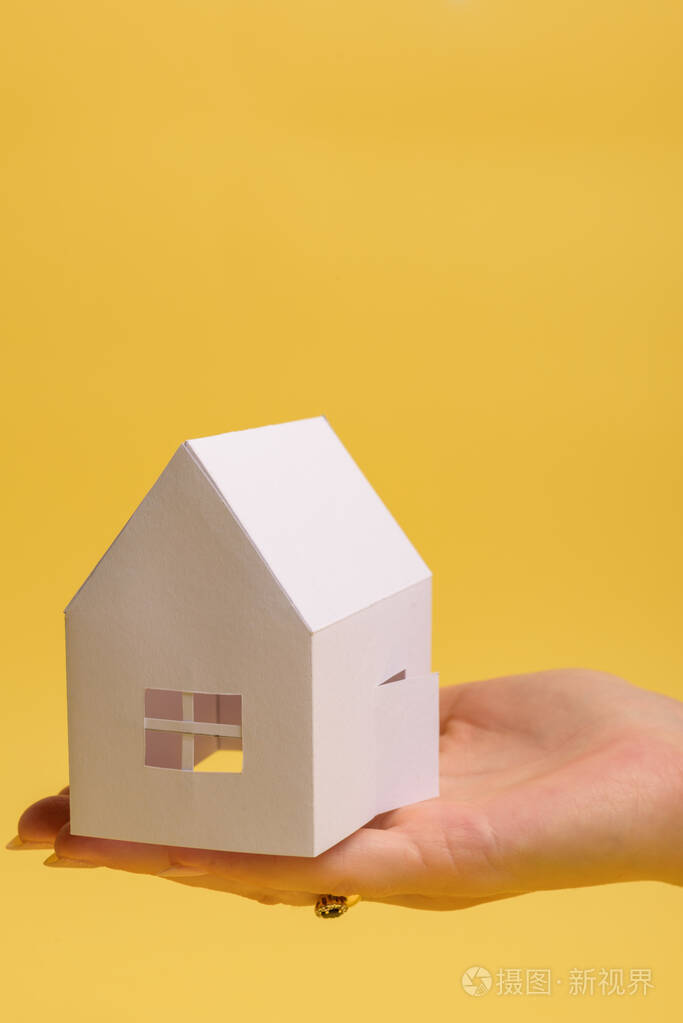 白色家庭纸房子在男人手上的黄色背景纸上简约风格复制空间从上面看