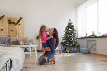 妈妈和女儿坐在圣诞树下的地板上拥抱。圣诞节早晨。在家过得愉快。
