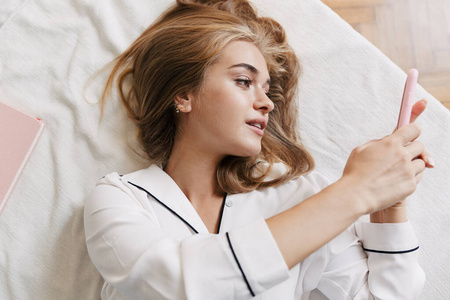 Image of pretty young girl holding cellphone while lying in bed 