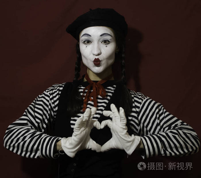 一个美丽的女孩在一个哑剧演员的形象从她的手折叠一个心脏看照相机.