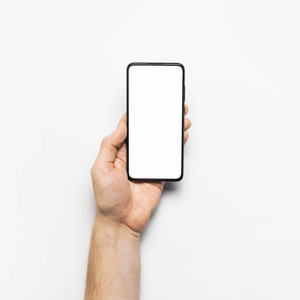 男性手持一部现代黑色智能手机，浅灰色背景下为白色空白屏幕。现代科技，手机，小玩意，触摸屏，设计模板。模型
