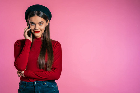 笑眯眯的潮人在粉色背景下用手机聊天.美丽的女人拿着和使用智能手机.