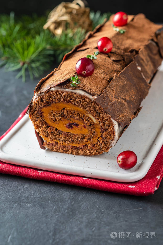 的圣诞甜点圣诞蛋糕巧克力奶油蔓越莓在石头灰色的背景和圣诞树的树枝