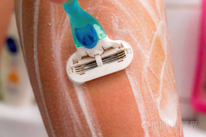 女孩用剃须刀刮腿毛在腿上撒上泡沫