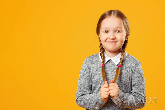 黄色背景下一个快乐的小女孩的特写肖像。一个女学生把头发梳成辫子，看着镜头。复制空间