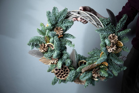 花匠手拿圣诞花环的特写镜头，花环上放着冷杉树枝和圆锥体。