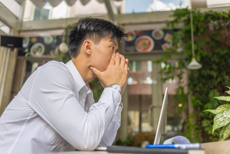 沮丧的亚洲商人坐在咖啡厅的笔记本电脑前