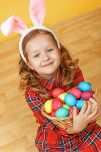 一个可爱的小女孩抱着一篮子复活节彩蛋坐在地板上