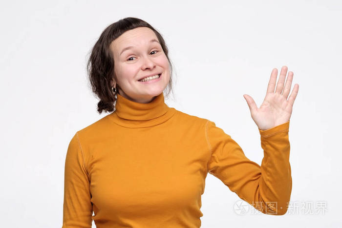 穿着黄色衣服的年轻白人妇女挥手向她的朋友问好或道别