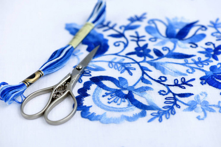 Embroidery, thread and scissors. Blue floral ornament on a white