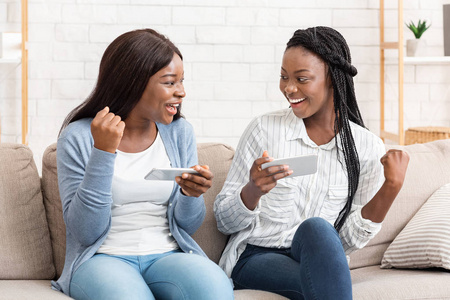 两个非洲女孩在智能手机上玩游戏庆祝胜利