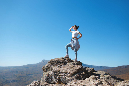 一个背着背包的女孩坐在山上的岩石上欣赏大自然的景色。