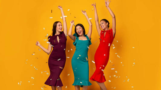 三个快乐的女孩在黄色背景下飘落的五彩纸屑下跳舞照片