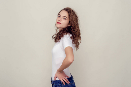 迷人的女孩侧身站在浅黄色的背景上,看着镜头.浅笑照片