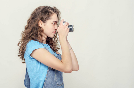 一个卷曲的黑发女孩穿着牛仔工作服,手里拿着一台老式胶卷相机.