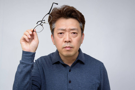 亚洲中年男性试图摘下眼镜看到一些东西.视力差,老花眼,近视.照片