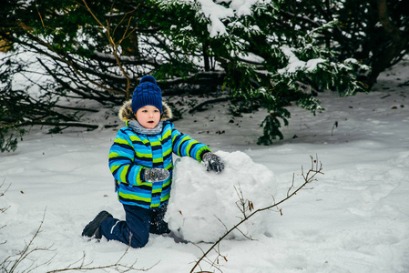 可爱的小男孩在堆雪人。滚大雪球