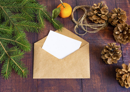 一张白色的白纸卡片，装在棕色手工信封里，放在一张圣诞风格的旧木桌上。桌上摆着冷杉树枝桂皮和球果。圣诞节和新年。