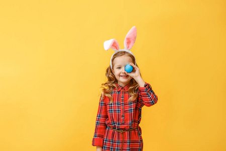快乐的小女孩，有兔子耳朵，彩色背景上有一个复活节彩蛋