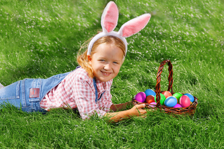 公园里绿草丛中，可爱的小女孩提着篮子。寻找复活节彩蛋的概念