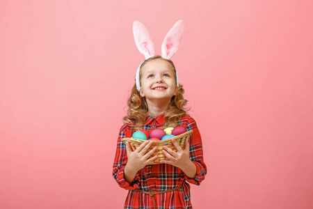 可爱的小女孩，有兔子耳朵，在彩色背景上拿着一篮子复活节彩蛋