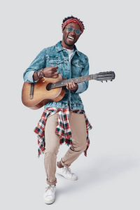 一个英俊的非洲年轻人在灰色背景下弹吉他，微笑着