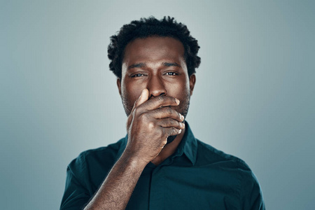 Handsome young African man looking at camera and covering mouth 